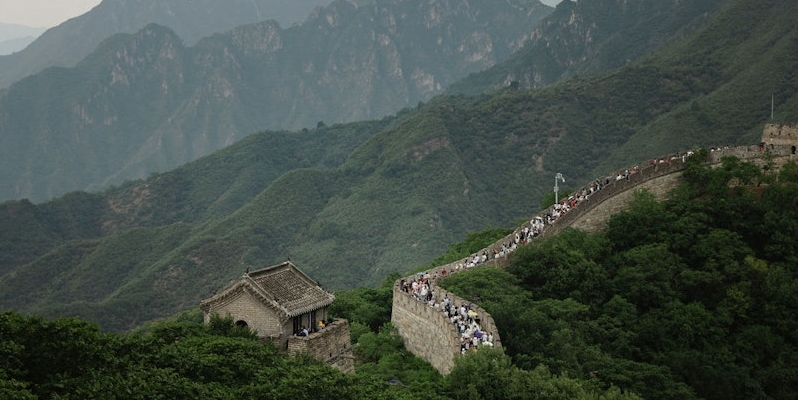 A section of the Great Wall of China runs through a lush, mountainous landscape, attracting many visitors walking along the wall. Plan your visit to China in 2024 and experience this breathtaking marvel firsthand.